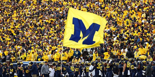 A cheerleader runs a Michigan Wolverines flag down the field after a touchdown during a game against the Penn State Nittany Lions at Michigan Stadium on October 15, 2022, in Ann Arbor, Michigan. 