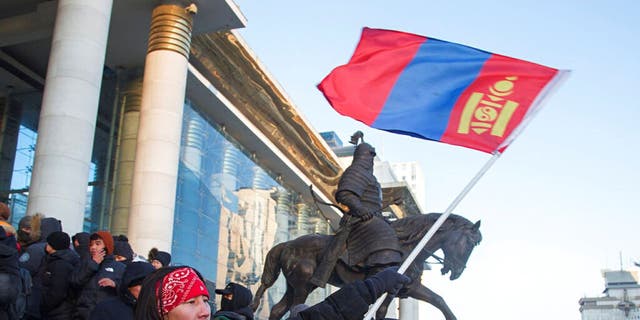 A protester waves a Mongolian national flag as protesters gather on the steps of the State Palace in Ulaanbaatar in Mongolia on Monday, Dec. 5, 2022. 