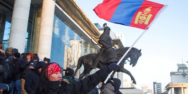 A protester waves a Mongolian national flag as protesters gather on the steps of the State Palace in Ulaanbaatar in Mongolia on Monday, Dec. 5, 2022. 