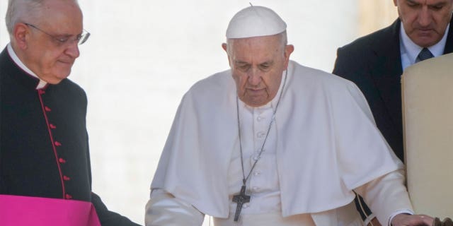 Pope Francis, center, walks with a cane to his weekly general audience with the help of his aide Monsignor Leonardo Sapienza, left, in St. Peter's Square at The Vatican, on June 1, 2022.