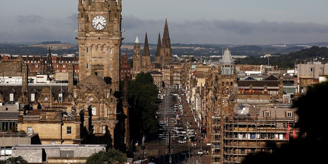 Vehicles drive down Princes Street as the clock tower of the Balmoral Hotel is visible on the city skyline in Edinburgh, UK.