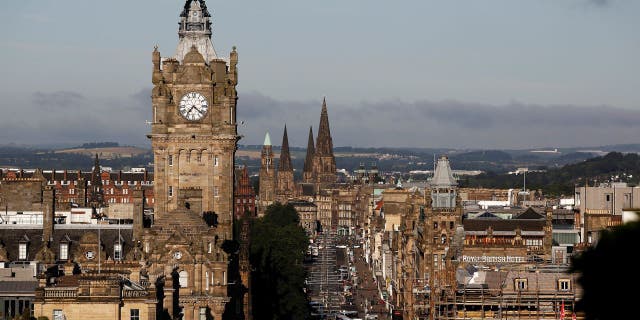 Vehicles pass along Princes Street as the clock tower of Balmoral hotel is seen on the city skyline in Edinburgh, U.K.