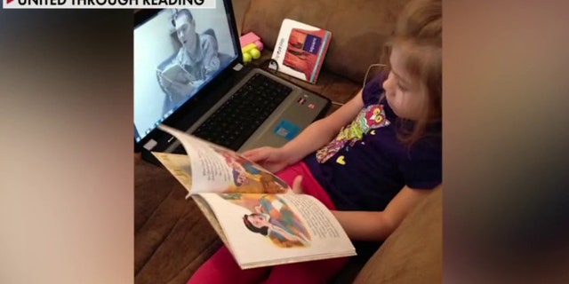A little girl reads along with her father who's deployed.