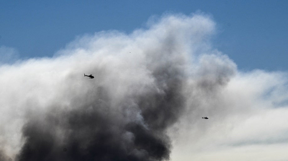 Two helicopters in the sky over a plume of smoke