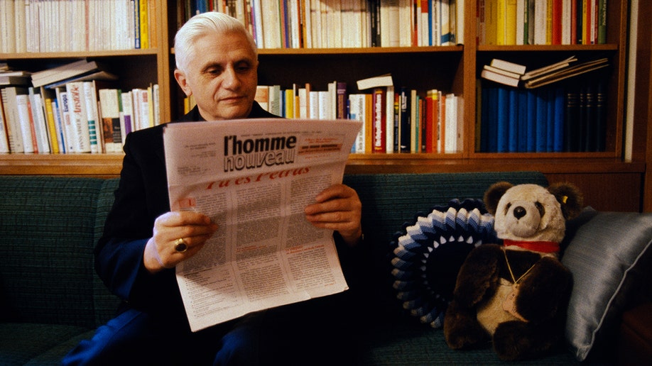 Former Pope Benedict reading a newspaper with a bear