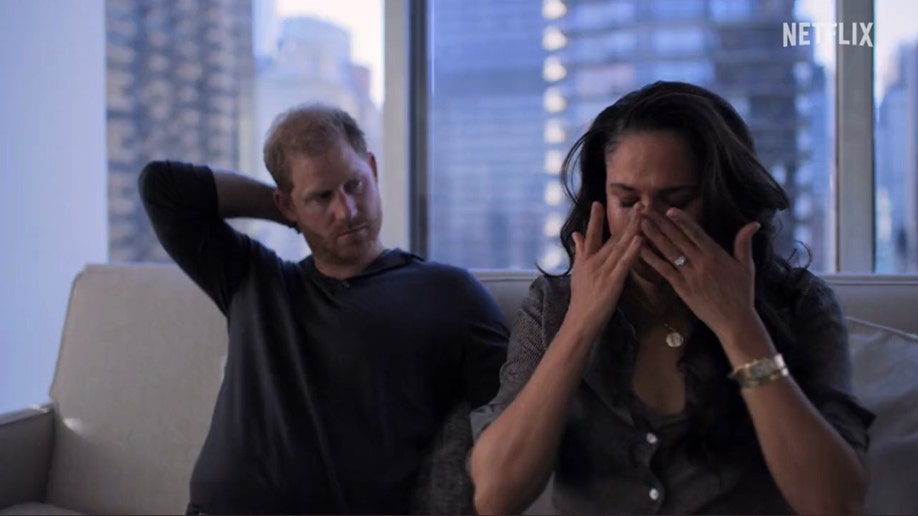 Meghan Markle cries on a couch and puts her hands to her eyes as Prince Harry looks at her with worry