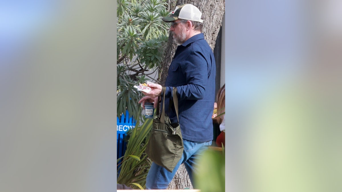 A man wearing a trucker hat and sunglasses carries food.