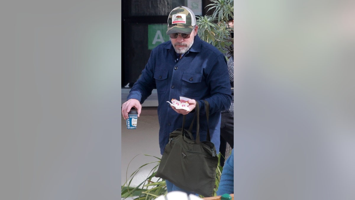 A man in a trucker hat and sunglasses carries food.