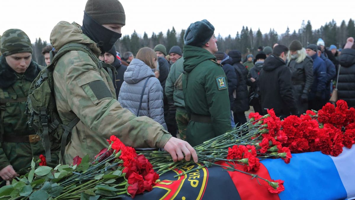 Wagner Group mercenary lays flowers on casket