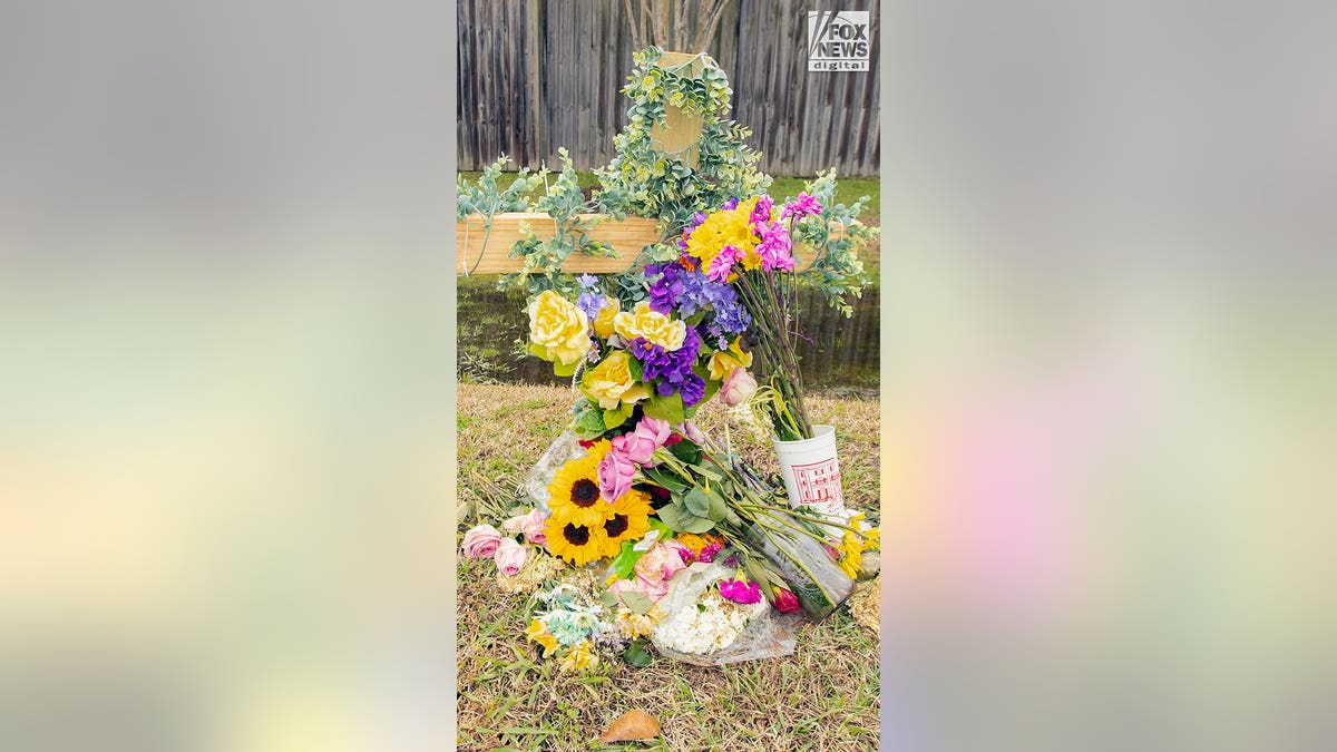 A small wooden cross covered with flowers by the side of a highway