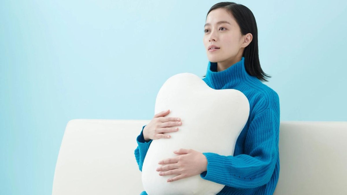 Woman in blue sweater hugs white pillow