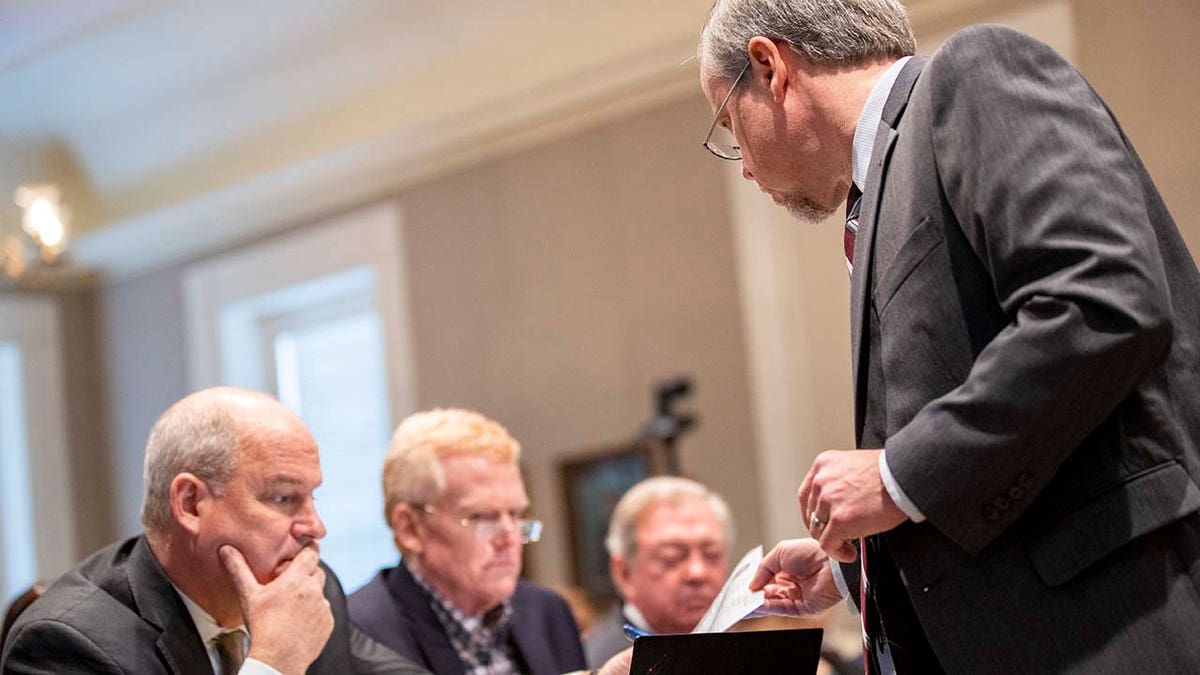 A man in a suit hands a piece of paper to a group of men.