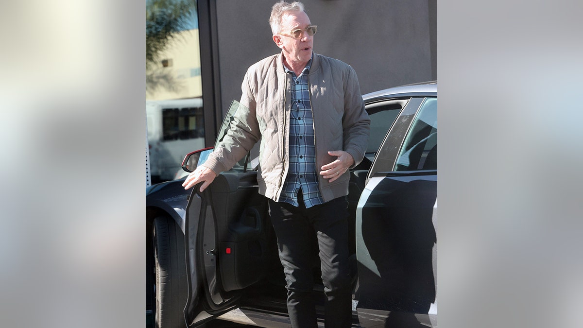 Tim Allen in a plaid blue shirt and grey jacket and black jeans gets out of his car wearing sunglasses