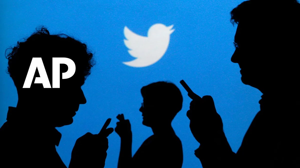 People holding mobile phones are silhouetted against a backdrop projected with the Twitter and AP logos