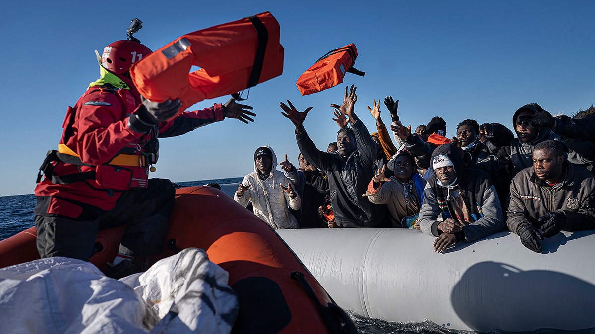 Coast guard throwing a red life jacket to migrants in a boat