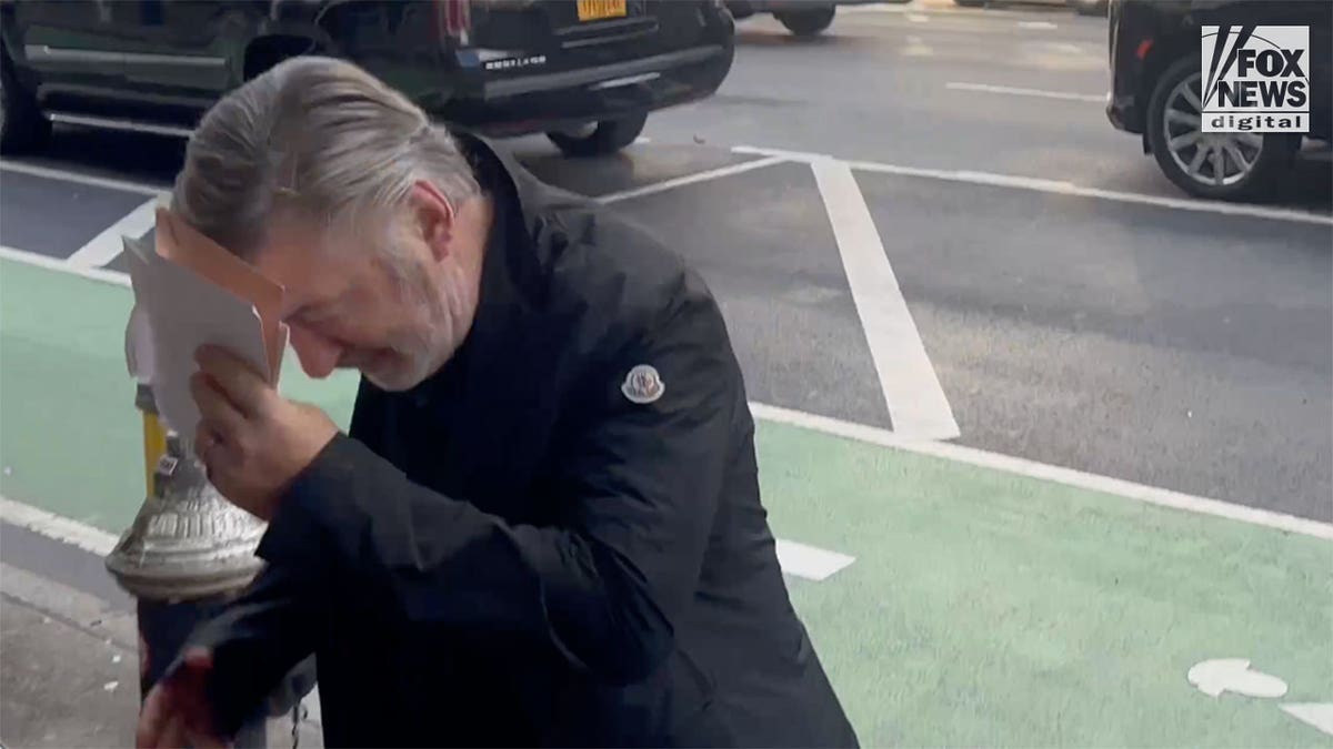 Alec Baldwin attempts to hide his face