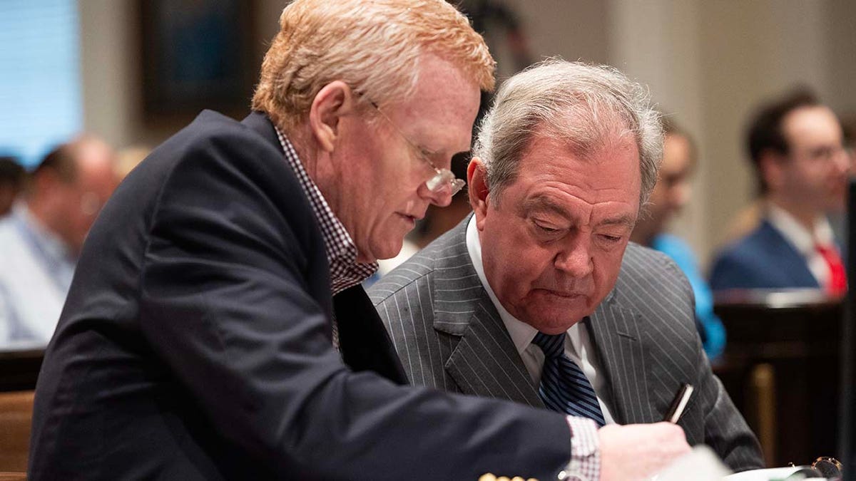 Two men look at documents inside a courtroom.