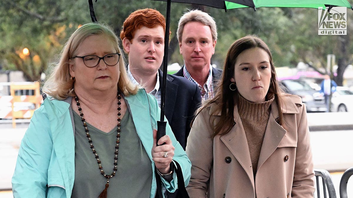 Four people holding an umbrella enter a courthouse.