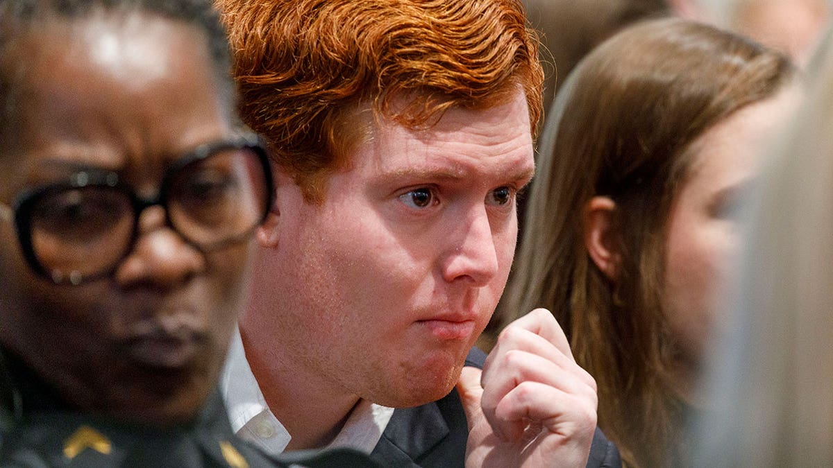 A man with red hair looks on while inside a courtroom.