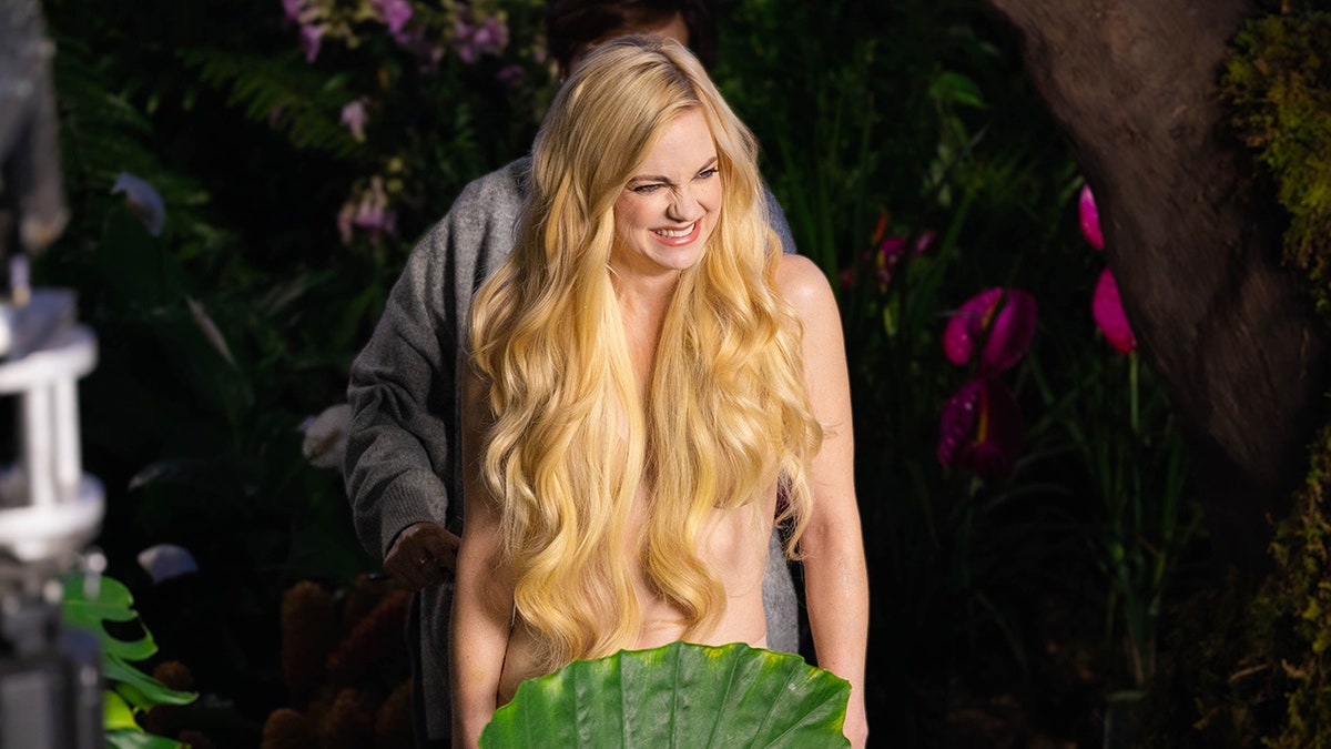Anna Faris smiles off camera while filming a Super Bowl ad, where her long blonde hair covers her chest and a leaf covers her bottom area