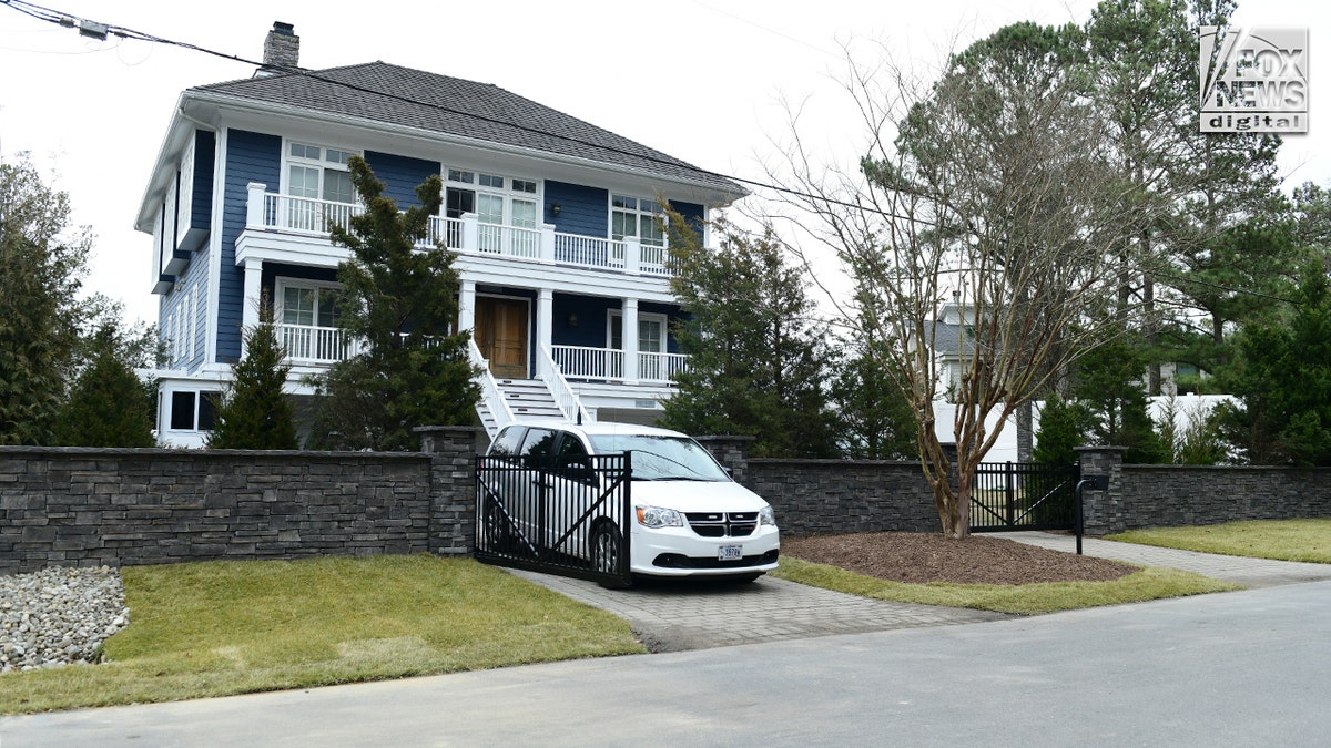 A street view of a blue house with a stone fence and white van parked outside.