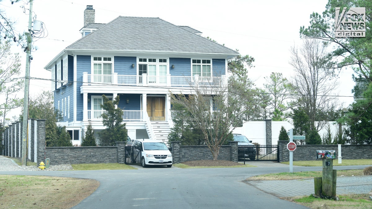 A blue, two-story house is surrounded by a stone and wooden fence.