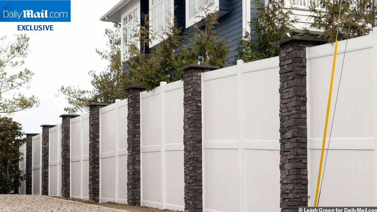 White wall with dark stone columns stretching down a gravel walkway.