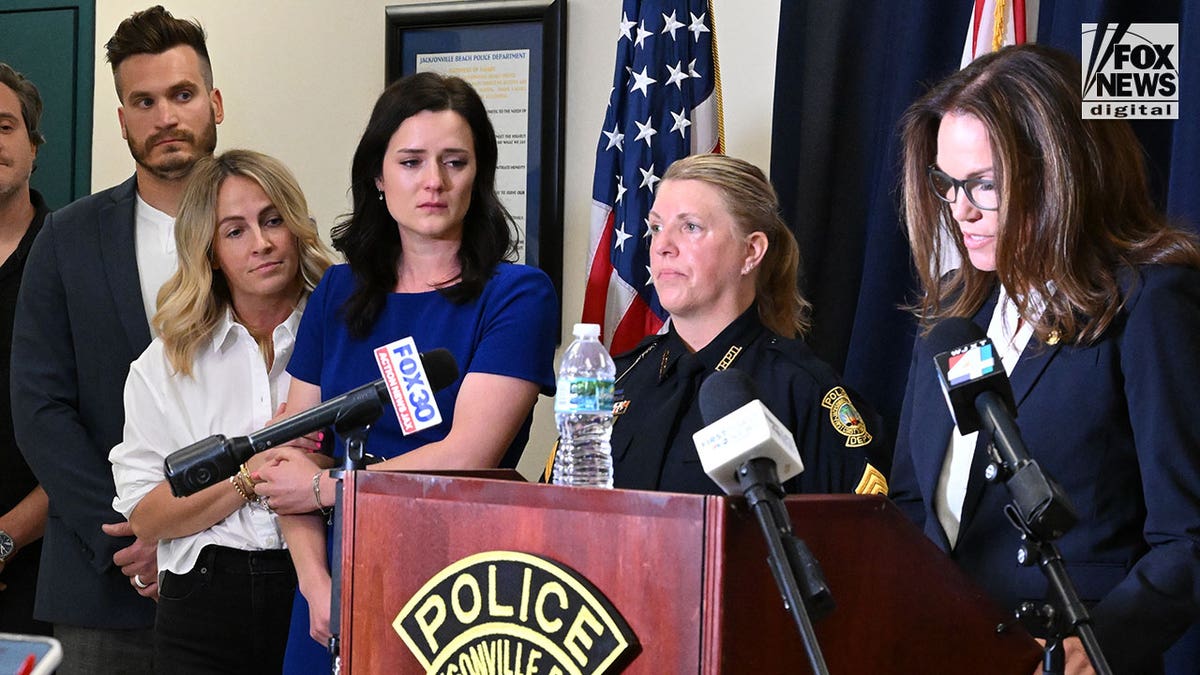 A police officer stands at a press podium surrounded by microphones.