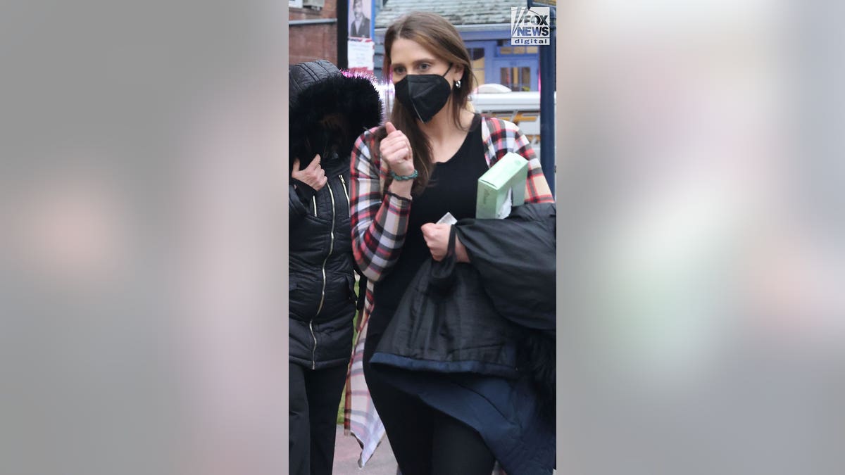 Woman in a plaid shirt and face mask clutches her coat and a box of tissues