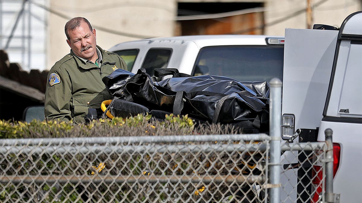 Sheriff rolling one of the victims in a body bag into a vehicle.