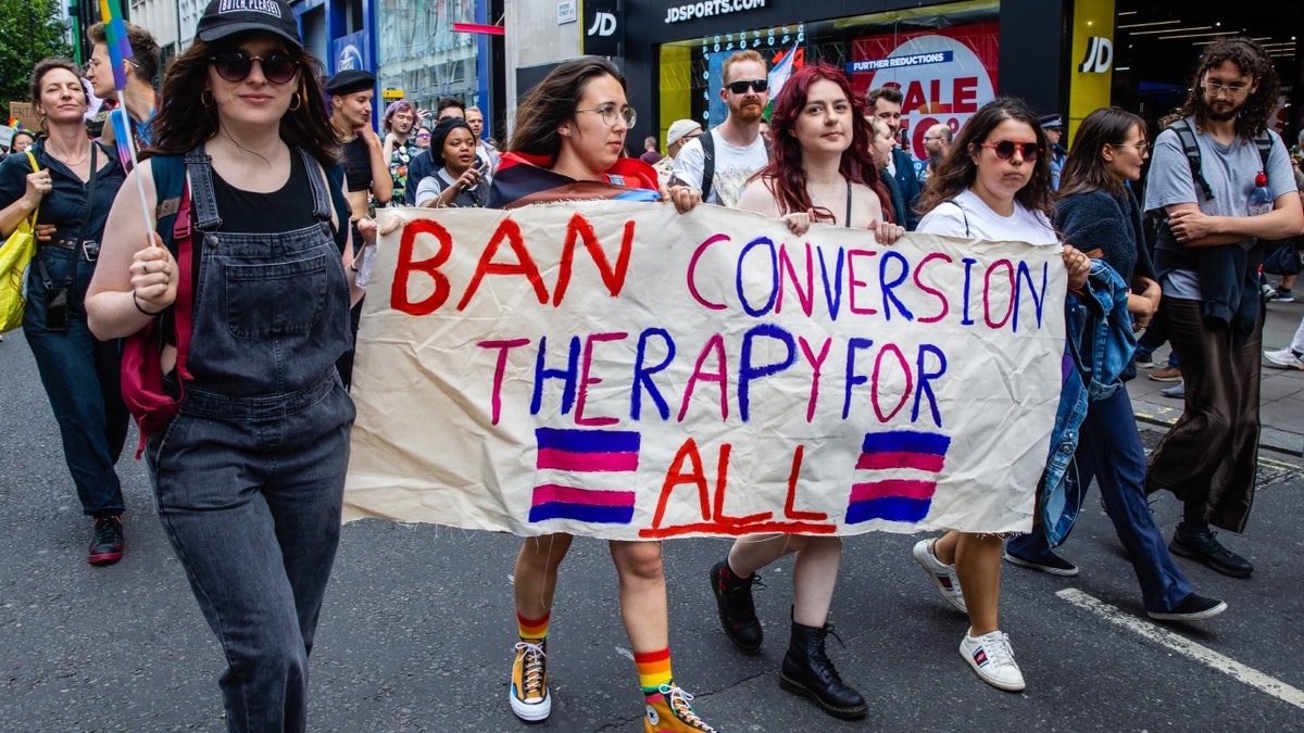 London Pride March participants holding sign reading "Ban Conversion Therapy for All"