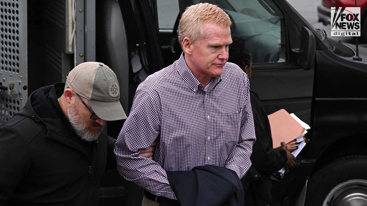 A man wearing a plaid shirt exits a police vehicle surrounded by officers.