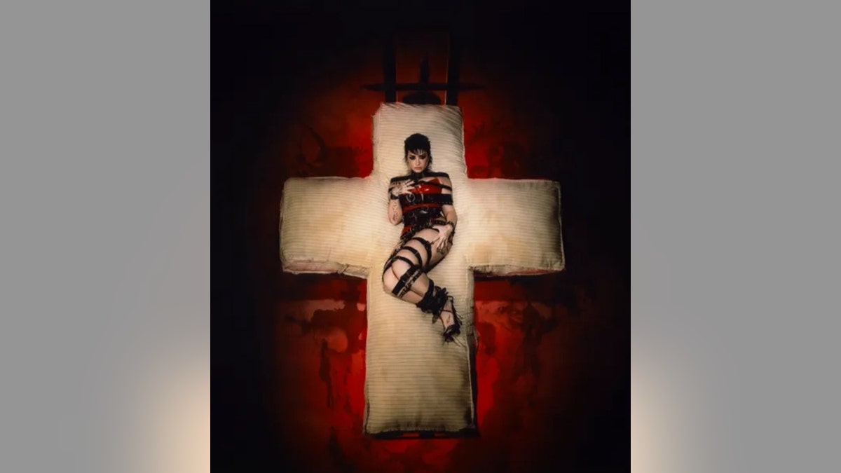 Demi Lovato lies on what appears to be a crucifex that is on the floor on top of a red sheet, and she wears black bondage