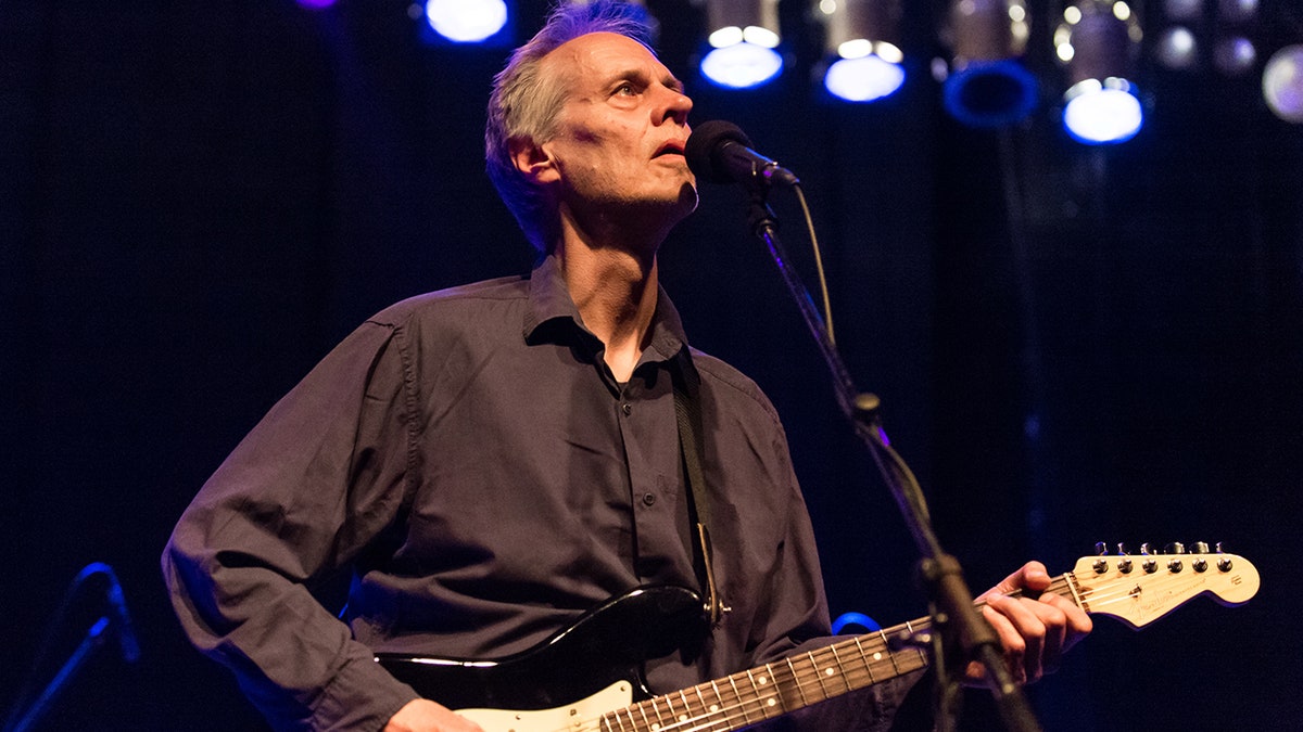 Tom Verlaine looks up as he sings and plays the guitar with Television on stage in 2019