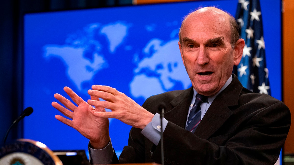 Elliott Abrams speaking in front of a giant blue map of the world