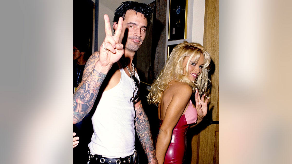 Pamela Anderson walks in a red and pink latex outfit while she holds Tommy Lee's hand who wears a white tank top