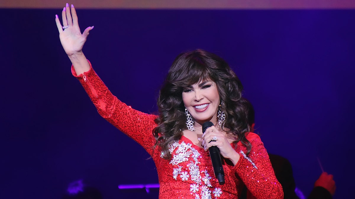 Marie Osmond in a sparkly red dress waves to the crowd while performing on stage
