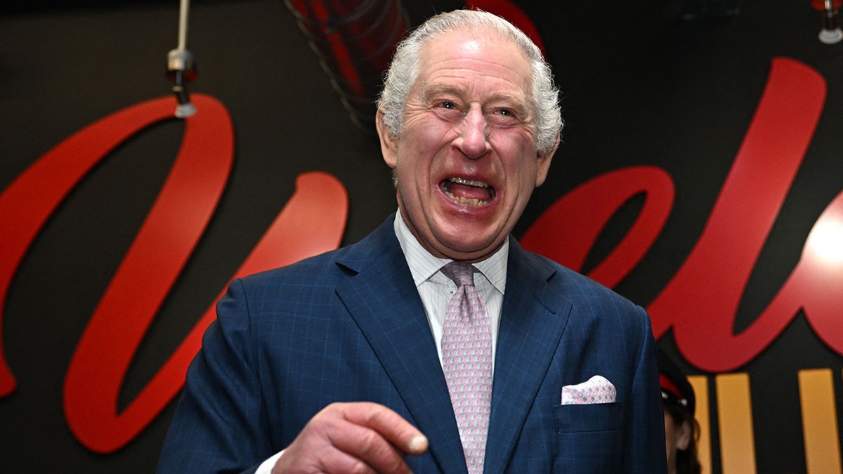King Charles laughs in a navy suit and light pink tie while in Manchester