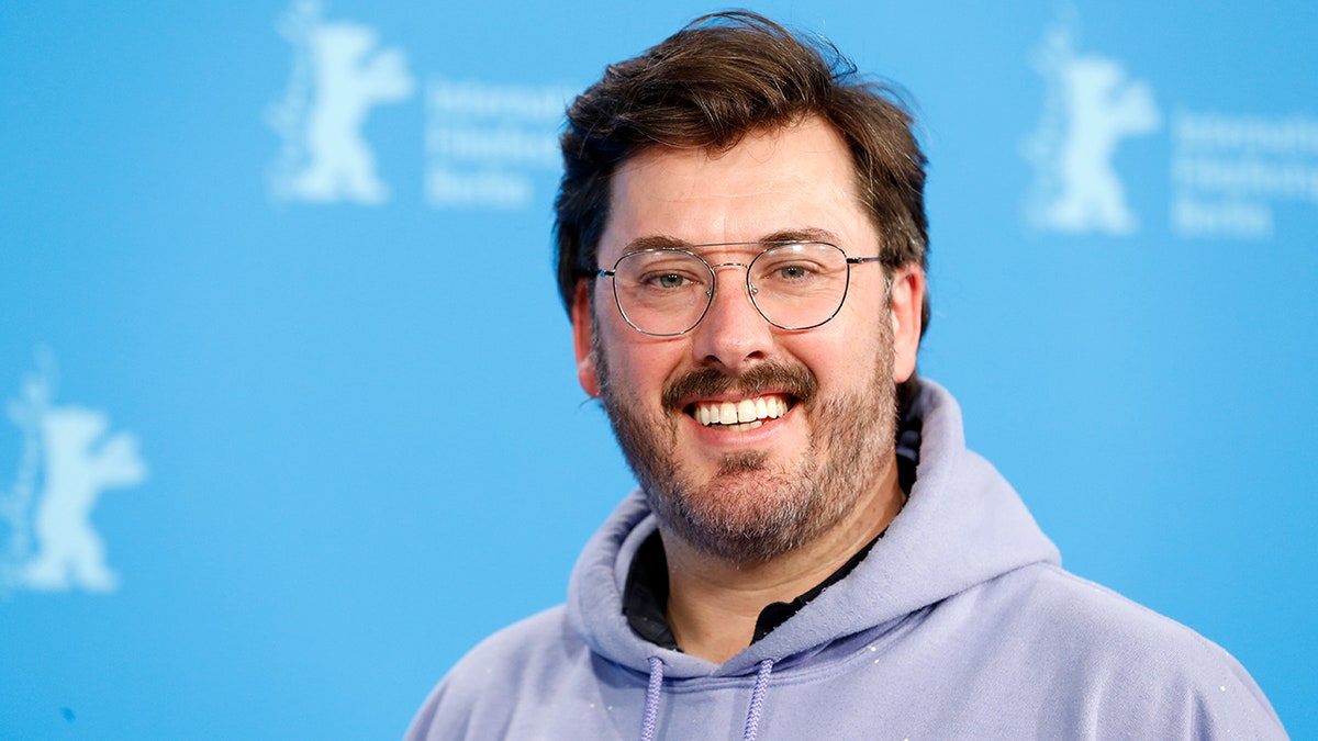 Ben Browning in a light purple sweatshirt with circular lightly rimmed glasses smiling on the red carpet