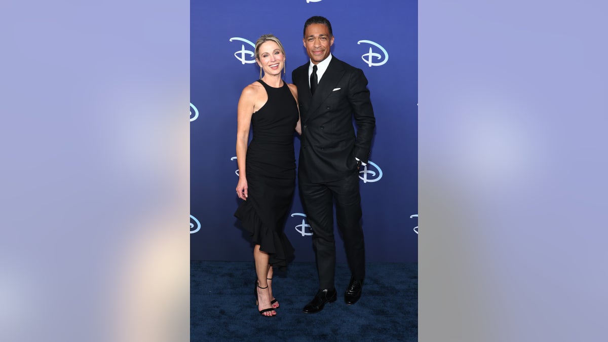 Amy Robach in a black long dress poses with T.J. Holmes in a suit on the red carpet