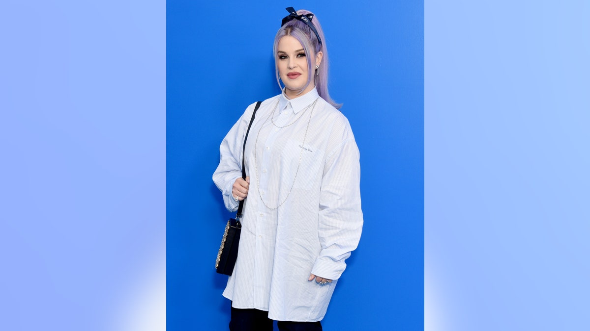 Kelly Osbourne in a white long blouse with her light purple hair tied up in a ponytail and bow