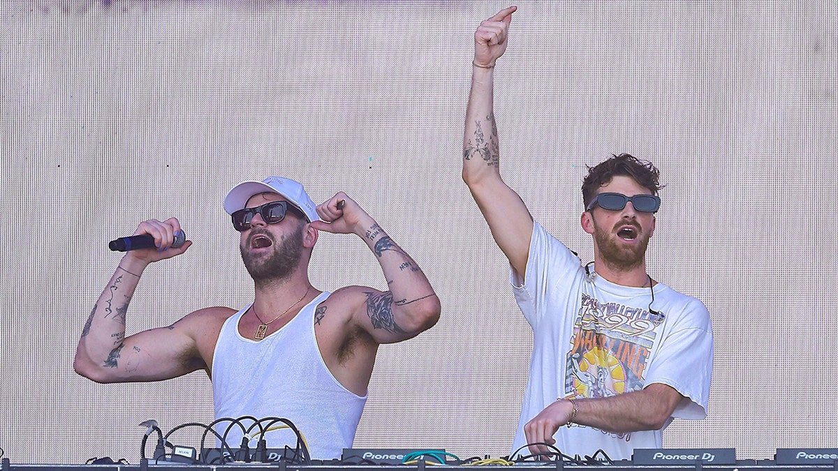 Alex Hall in a white tank top and hat with sunglasses performs on stage with Drew Taggar in a white t-shirt and sunglasses