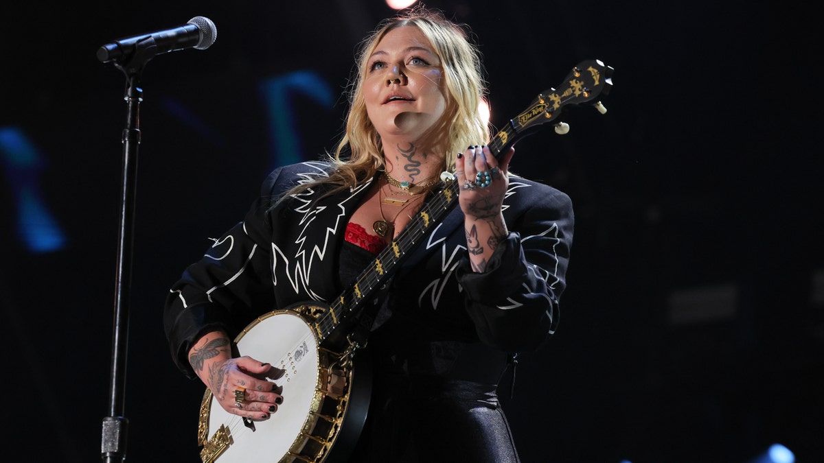 Elle King in a black leather jacket playing the banjo on stage