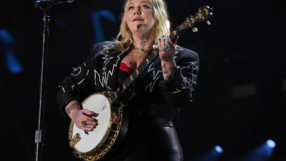 Elle King in a black leather jacket playing the banjo on stage