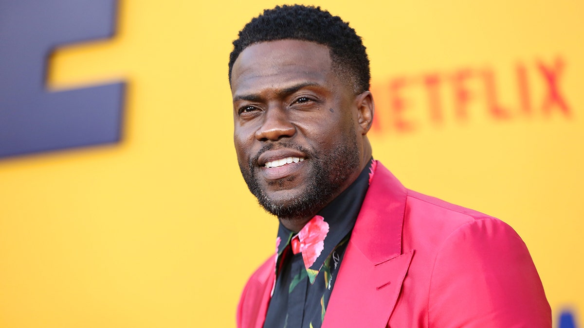 Kevin Hart with a black printed floral shirt and hot pink suit on the red carpet