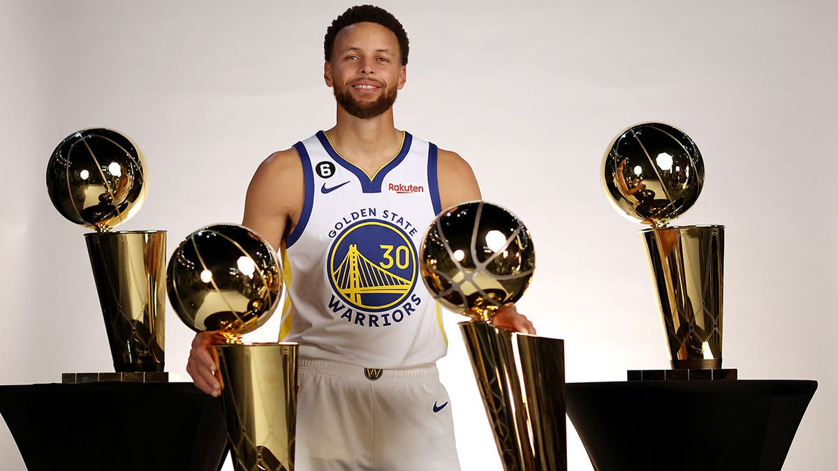Stephen Curry stands with his four championship trophies