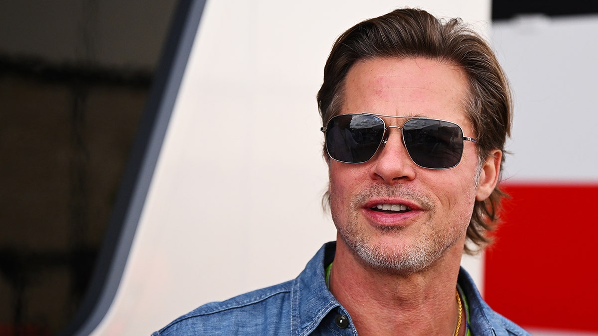 Brad Pitt in a jean shirt and dark shade sunglasses at the Formula 1 race