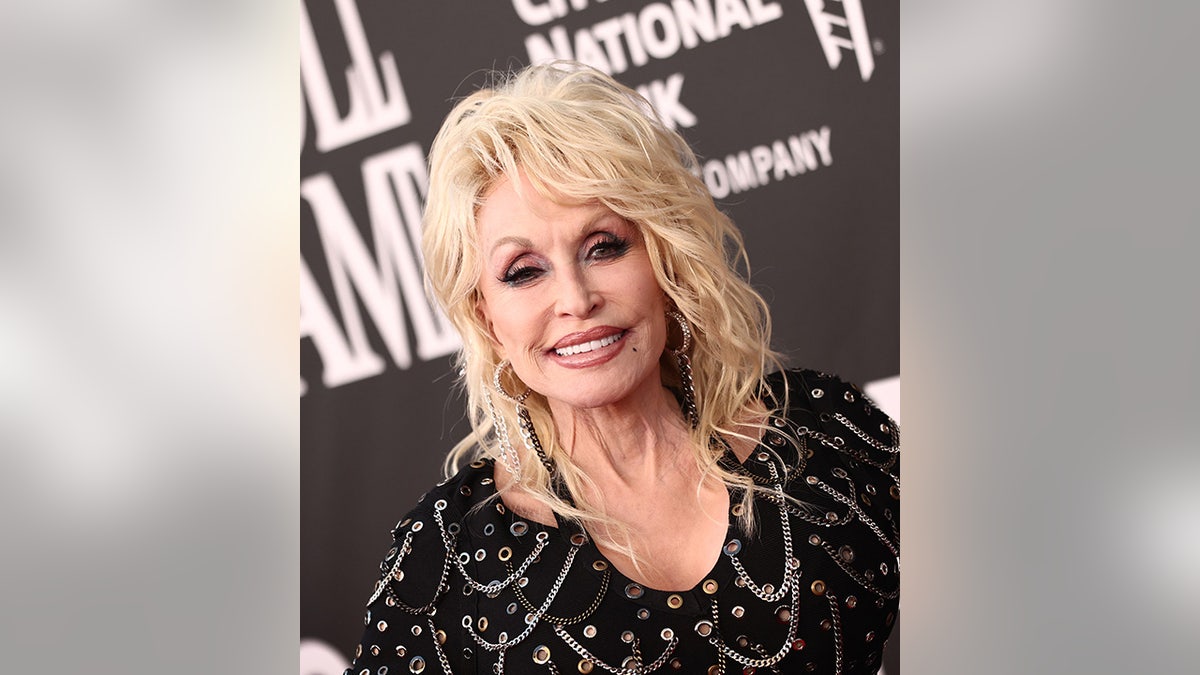 Dolly Parton in a black dress adorned with chains and sparkles on the red carpet for The Rock and Roll Hall of Fame