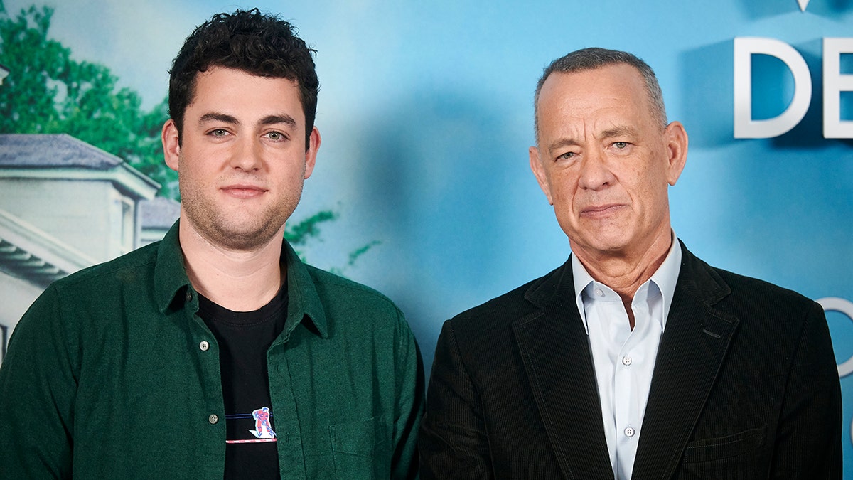 Truman hanks in a green button down shirt poses next to his father Tom Hanks with a light blue shirt and black suit jacket