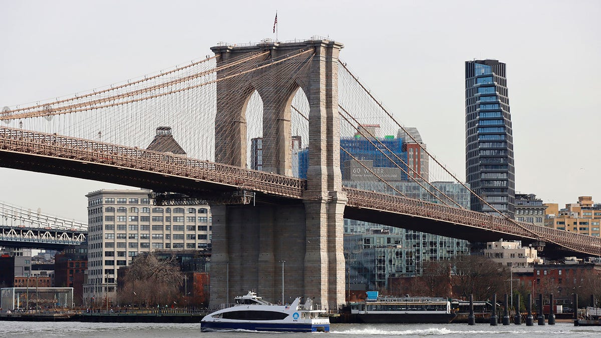 ferry sails by Brooklyn bridge